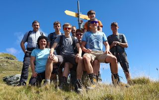 Team Holzmock auf Bergtour Berglialp, Gipfelfoto nach anstregendem Aufstieg, die Personen sind leicht verschwitzt